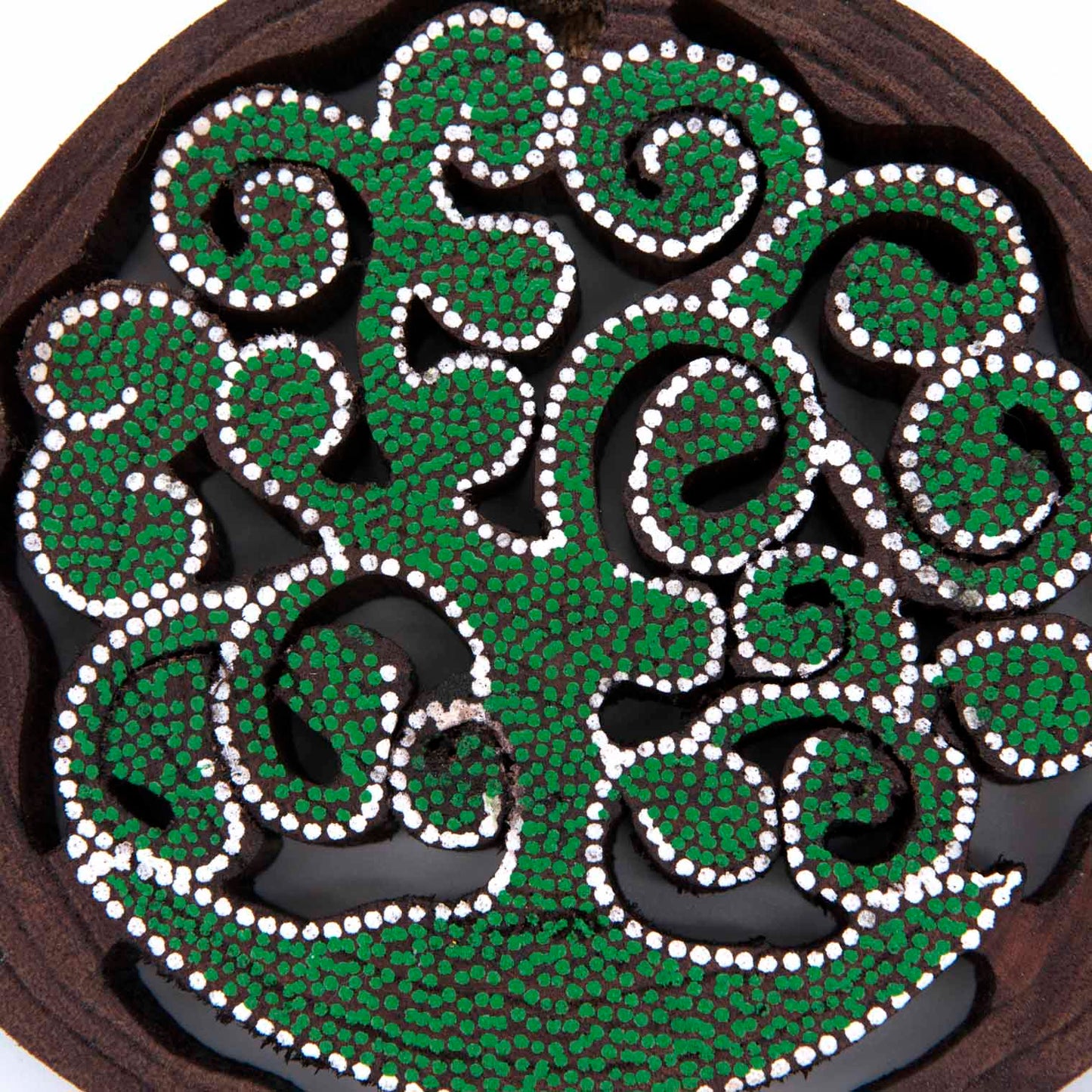 Close-up of dot-painted tree of life cutaway showing dense green and white dot pattern on dark wood, Indonesia