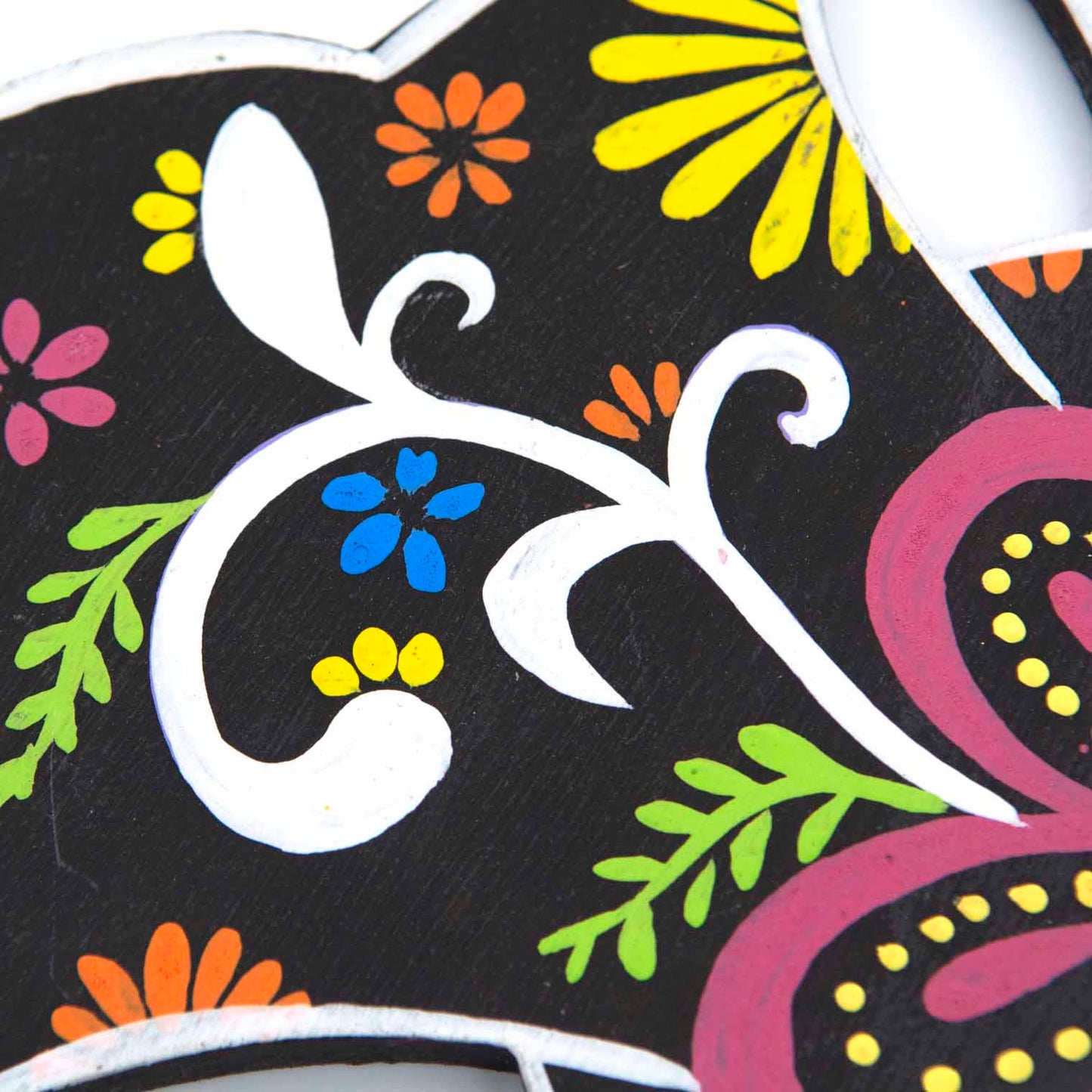Close-up detail of hand-painted wood cross showing white scroll stems, yellow daisy and blue flower motifs