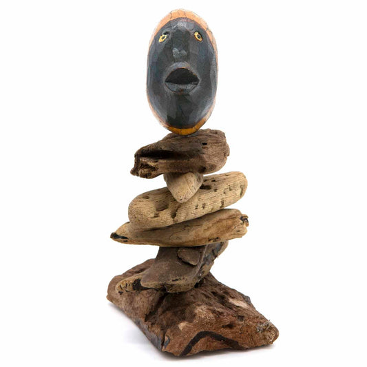 Carved painted face mask on driftwood stack, dark grey with gold eyes, Indonesia