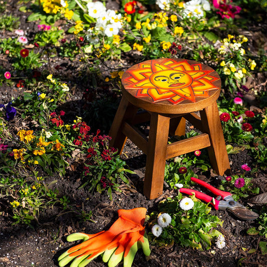 Raintree wood sun face stool with carved orange and yellow rays, set among garden flowers, northern Thailand