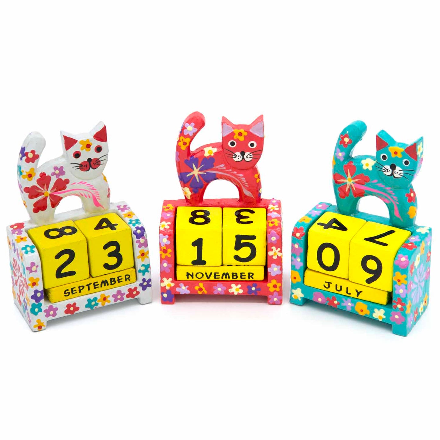Three painted wooden cat calendars side by side in white, red and teal colourways, Indonesia