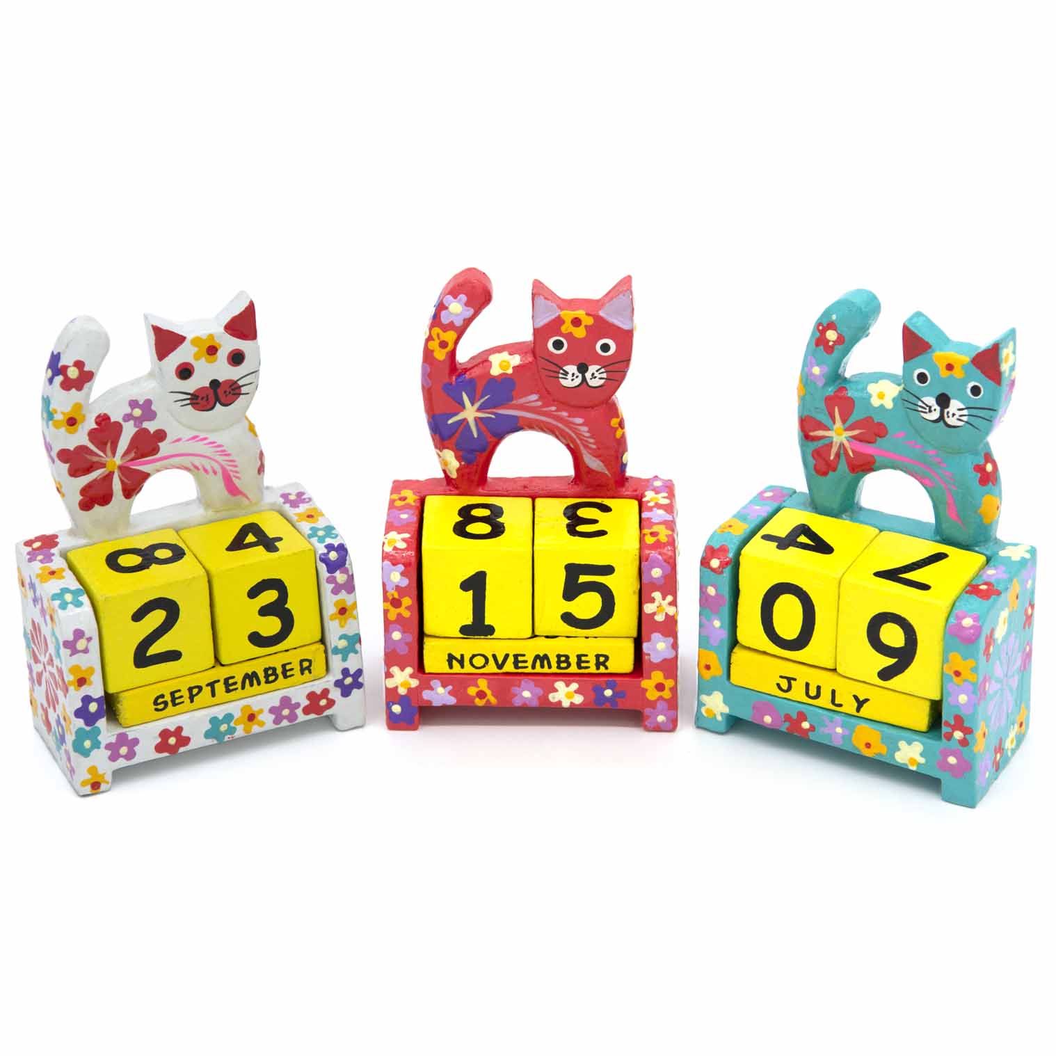 Three painted wooden cat calendars side by side in white, red and teal colourways, Indonesia