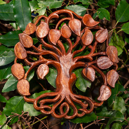 Circular carved wood tree of life plaque with heart-shaped leaves, warm reddish-brown grain, Bali Indonesia, set against real