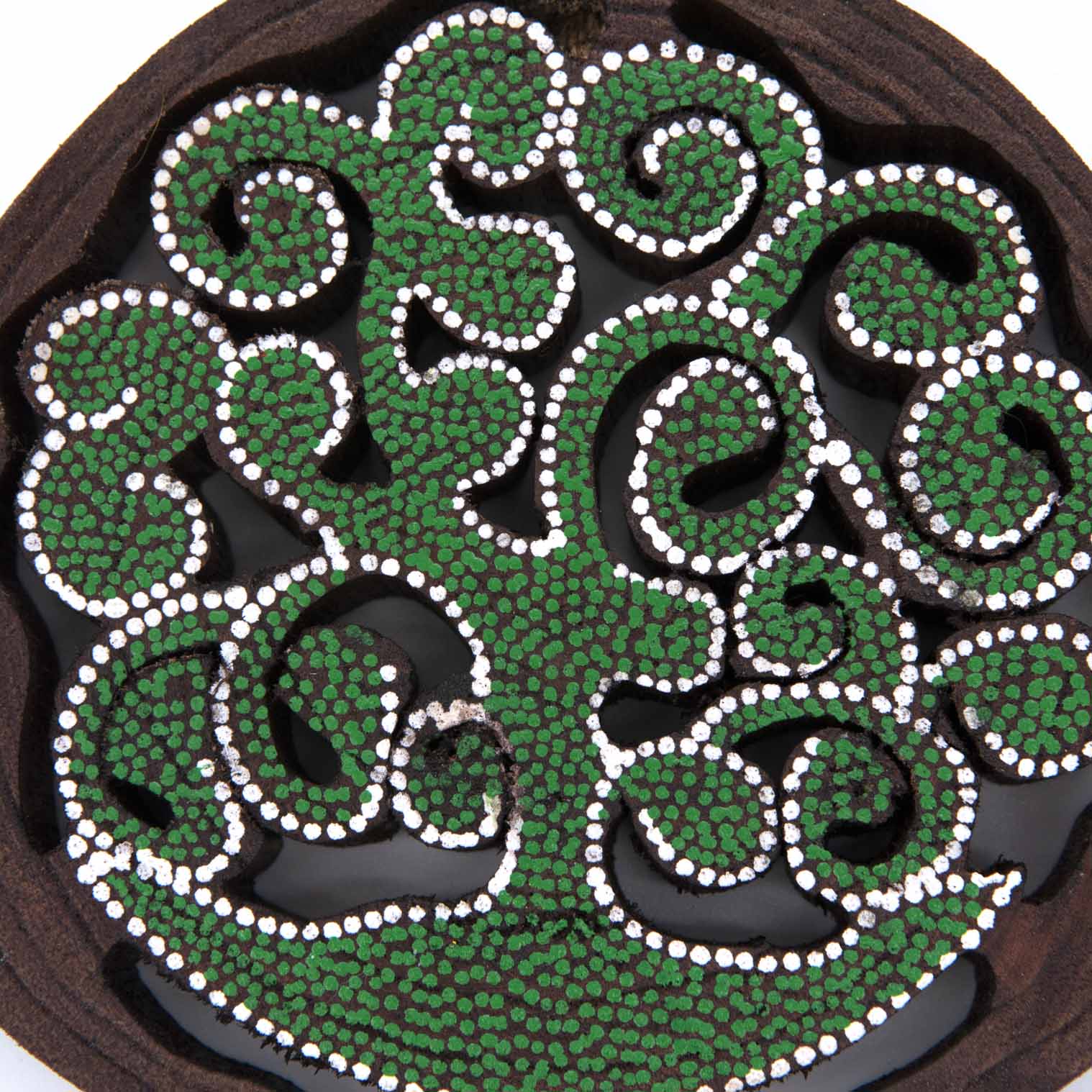 Close-up of dot-painted tree of life cutaway showing dense green and white dot pattern on dark wood, Indonesia