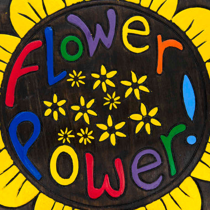 Close-up of Flower Power plaque centre showing carved multicolour lettering and yellow daisy motifs on dark wood grain