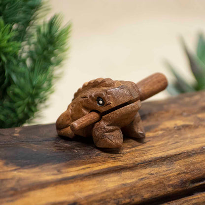 Mini acacia wood frog guiro with striker, front three-quarter view on wooden surface, northern Thailand