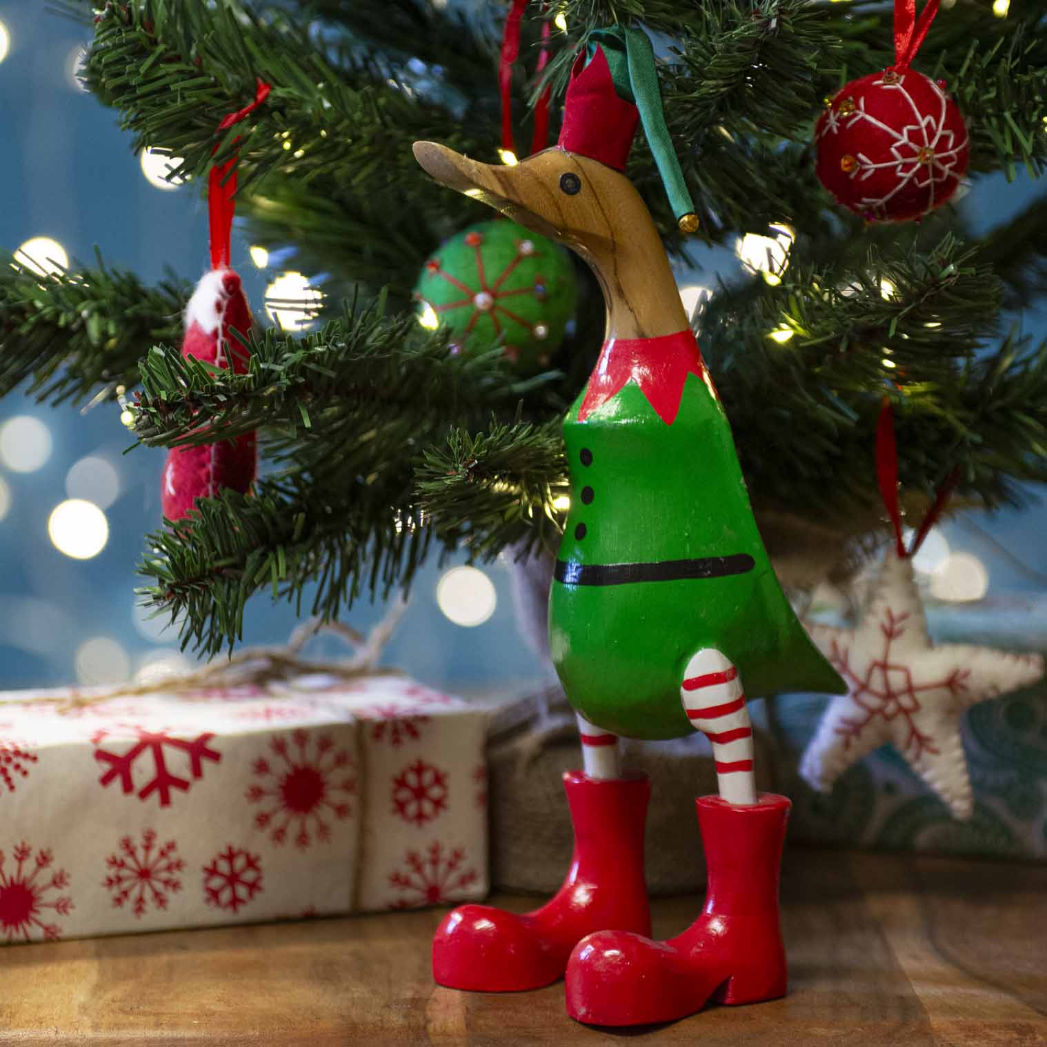 Bamboo root Christmas elf duck in green tunic and red boots standing under a lit Christmas tree, Bali Indonesia