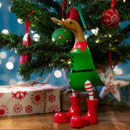 Bamboo root Christmas elf duck in green tunic and red boots standing under a lit Christmas tree, Bali Indonesia