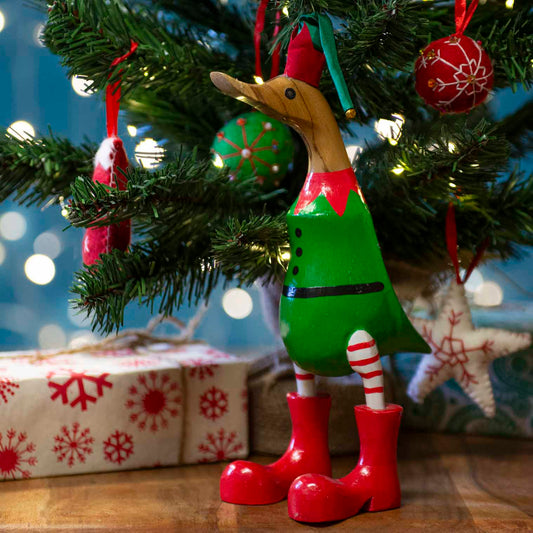 Bamboo root Christmas elf duck in green tunic and red boots standing under a lit Christmas tree, Bali Indonesia