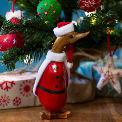 Small bamboo root Santa duckling in red coat with fleece trim standing under a lit Christmas tree, Bali Indonesia