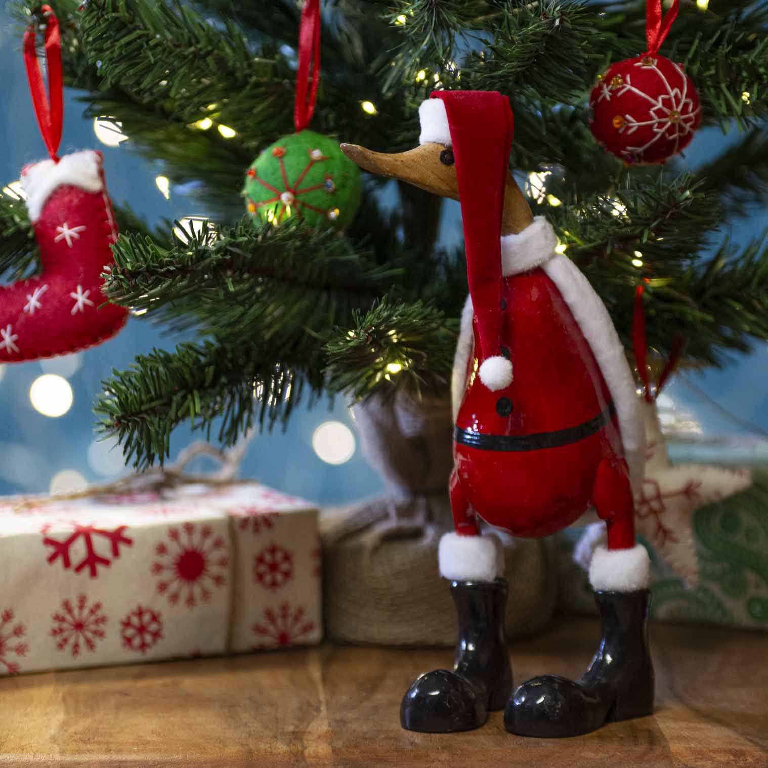 Large bamboo root Santa duck in red coat and black boots standing under a lit Christmas tree, Bali Indonesia