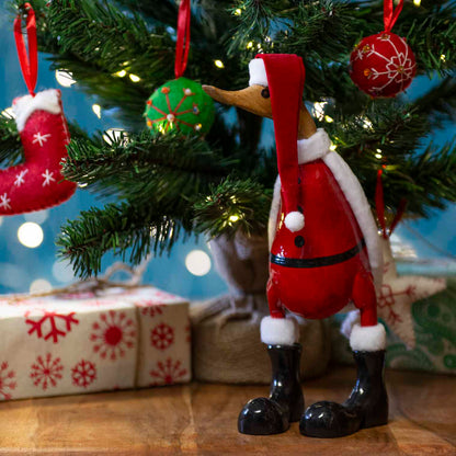 Large bamboo root Santa duck in red coat and black boots standing under a lit Christmas tree, Bali Indonesia