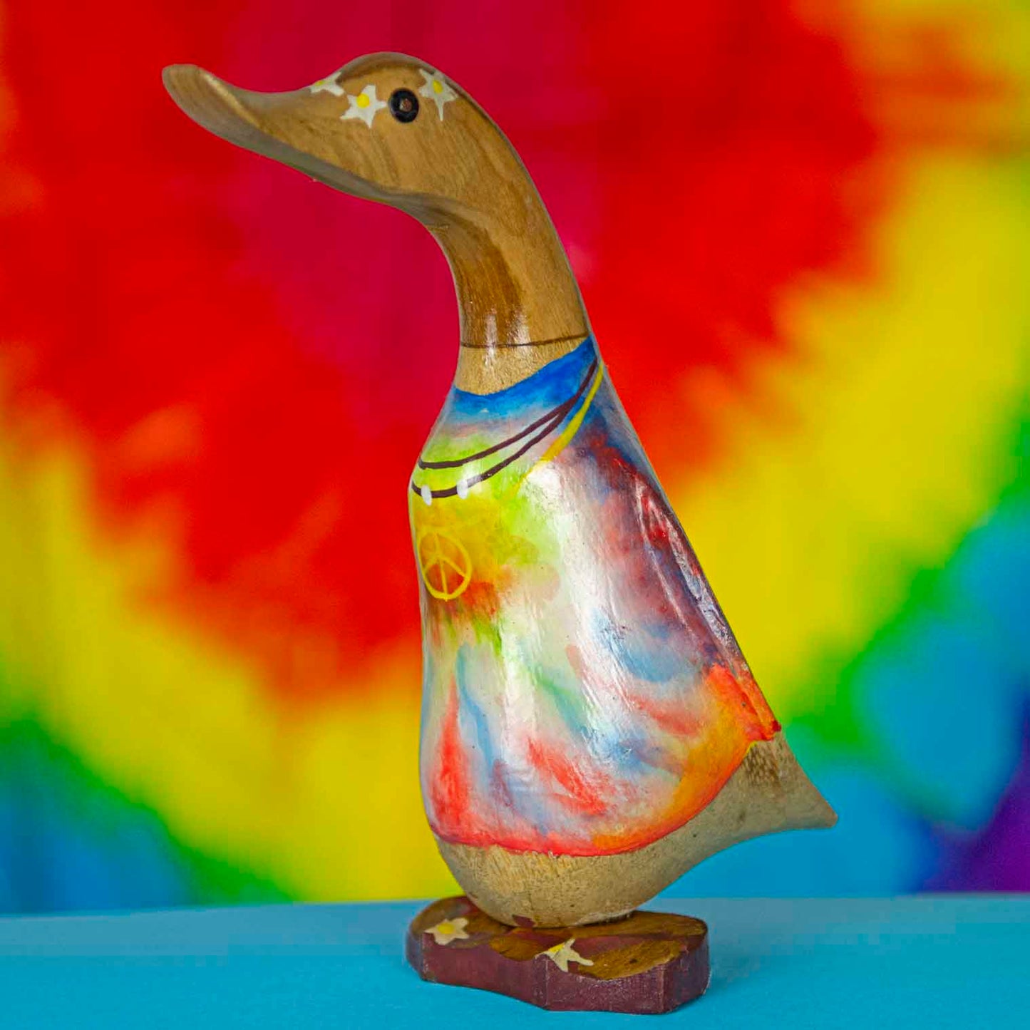 Tie-dye painted bamboo root duck from Bali, front three-quarter view against rainbow background