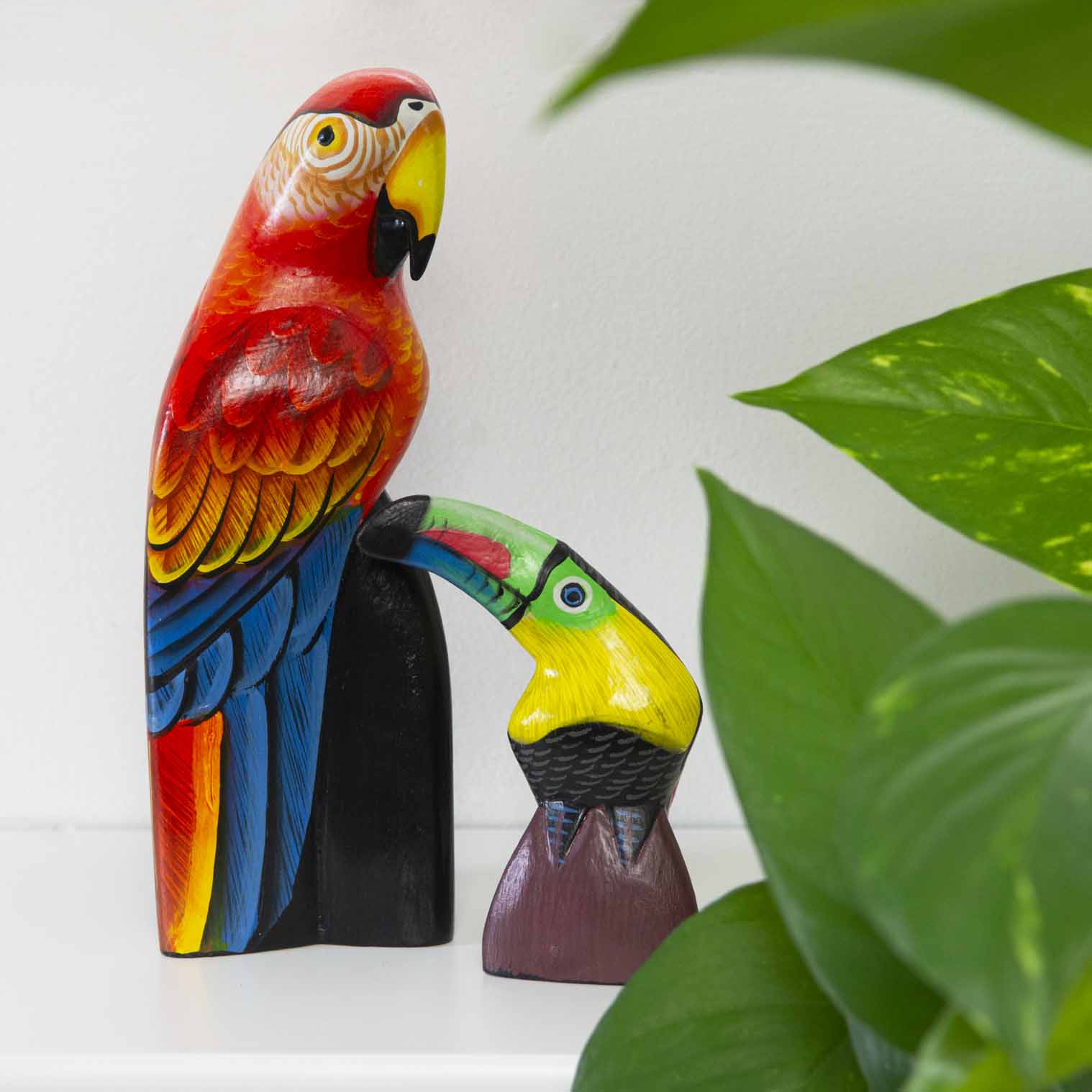 Hand-painted wooden toucan and parrot carvings on a shelf beside a houseplant, Indonesia