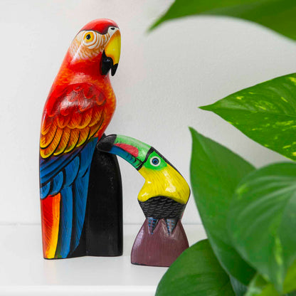 Hand-painted wooden toucan and parrot carvings on a shelf beside a houseplant, Indonesia