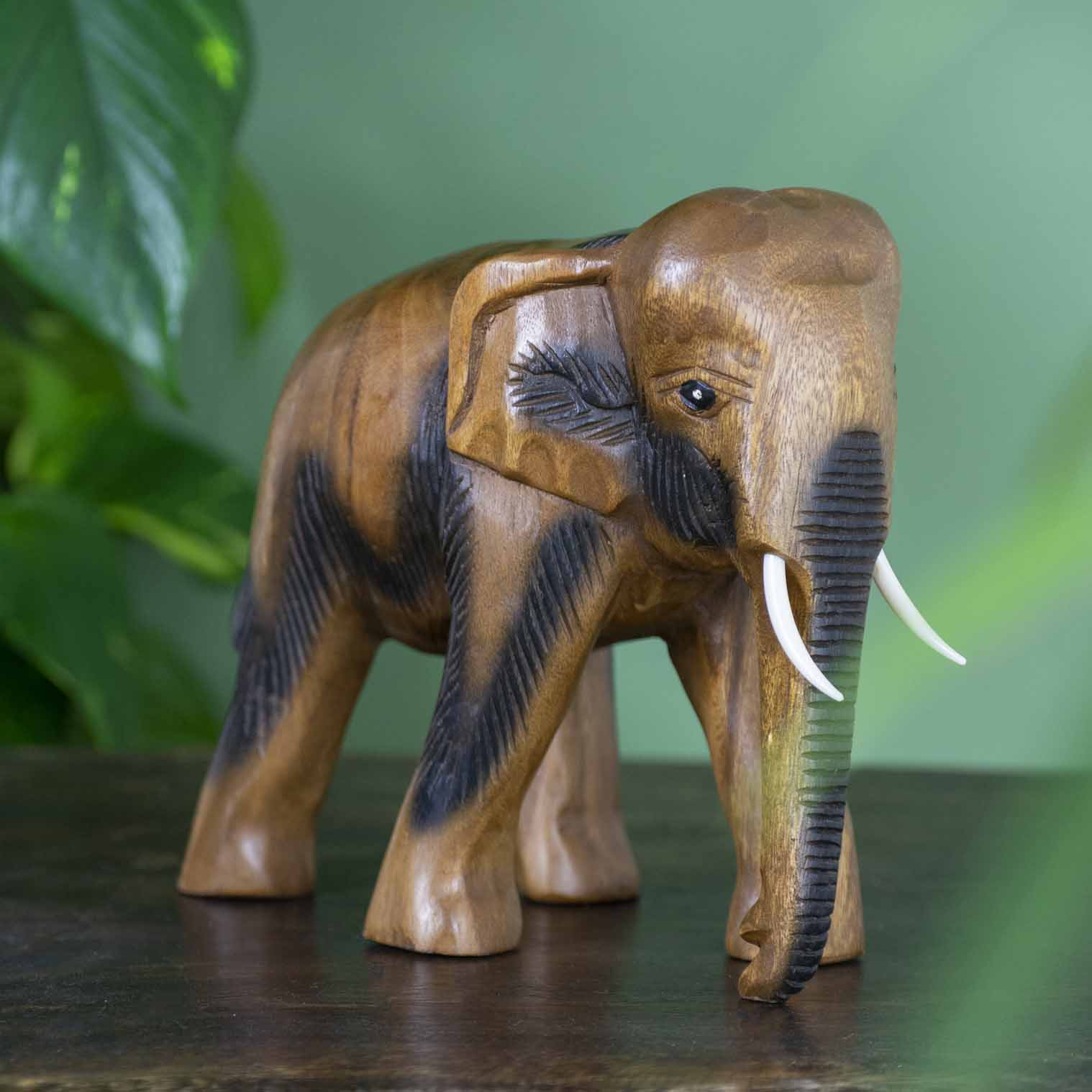 Large hand-carved Raintree elephant figurine with ribbed trunk detail, side view on dark surface, Thailand
