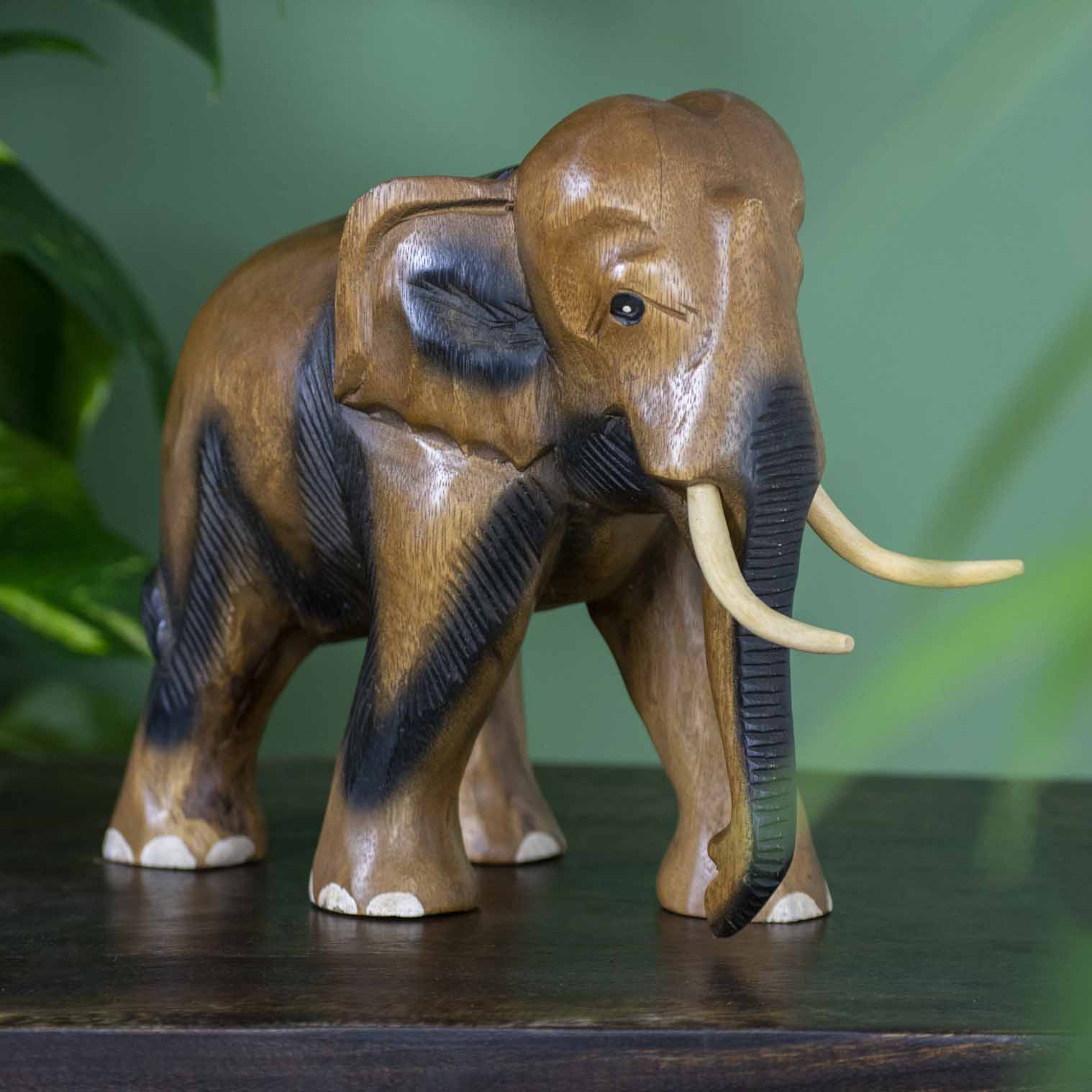 Extra large hand-carved Raintree elephant with painted toenails and ribbed trunk, side view on dark surface
