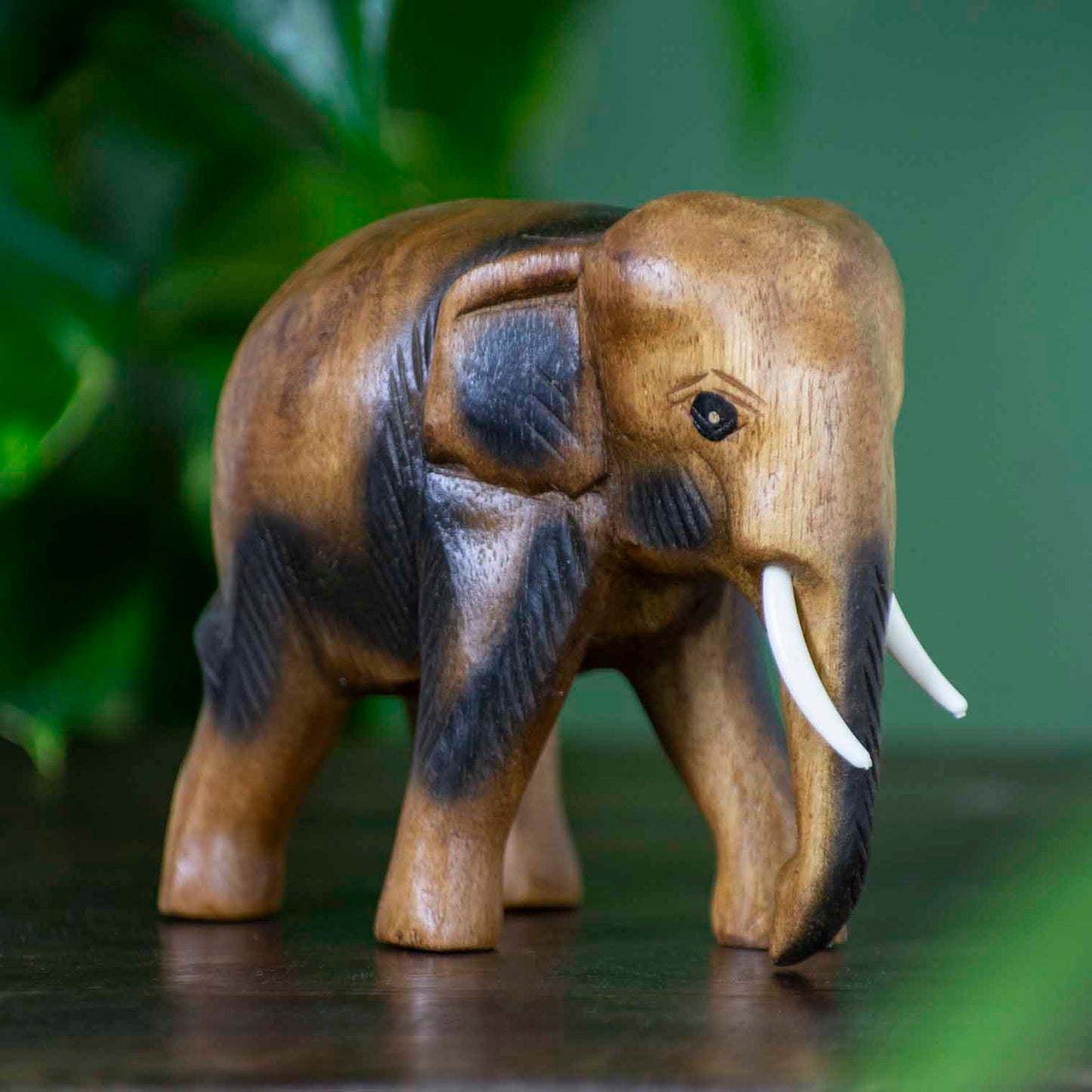 Medium hand-carved Raintree elephant figurine with warm golden-brown grain, side view on dark surface, Thailand