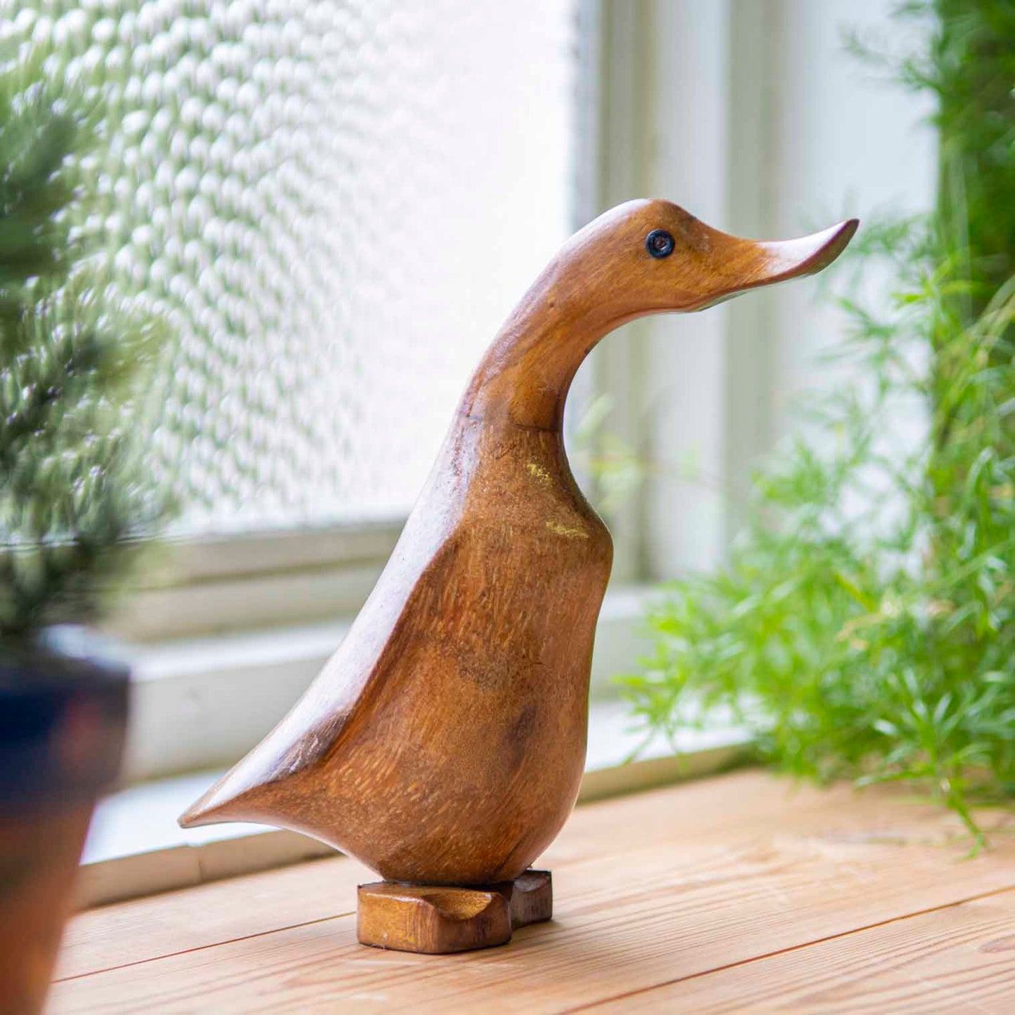 Side view of bamboo root duck carving on a wooden windowsill, showing warm grain and flat carved feet