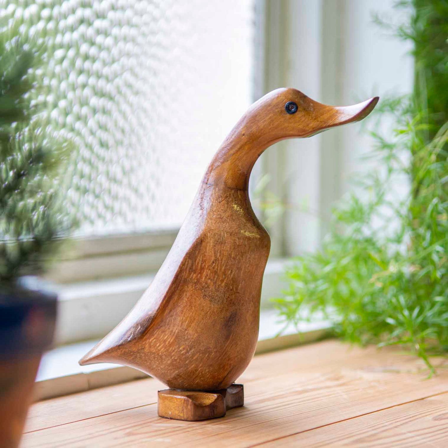 Side view of bamboo root duck carving on a wooden windowsill, showing warm grain and flat carved feet