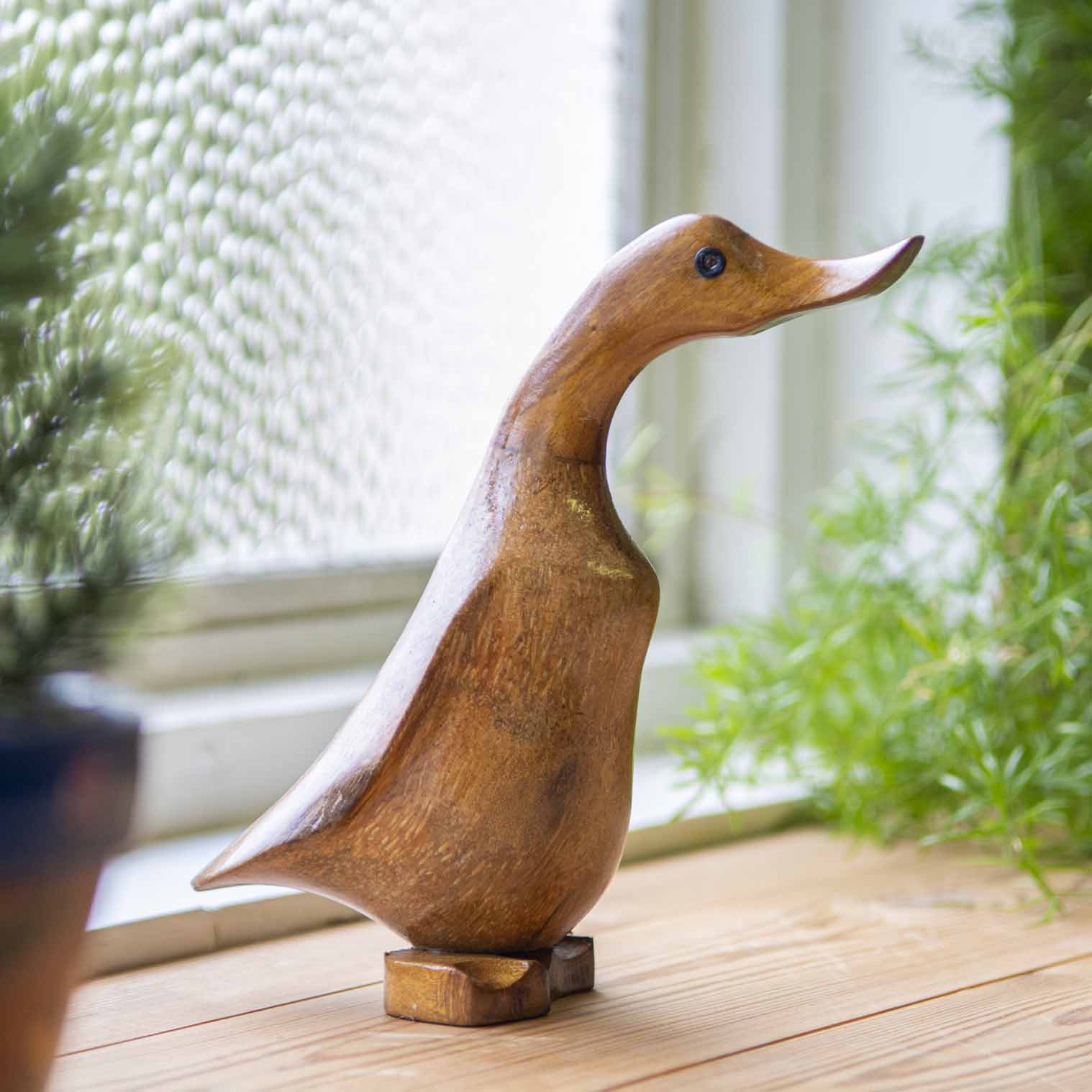 Side view of bamboo root duck carving on a wooden windowsill, showing warm grain and flat carved feet