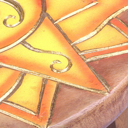 Close-up of carved sun ray detail on Raintree wood stool seat, showing gold-lined relief carving and orange paint