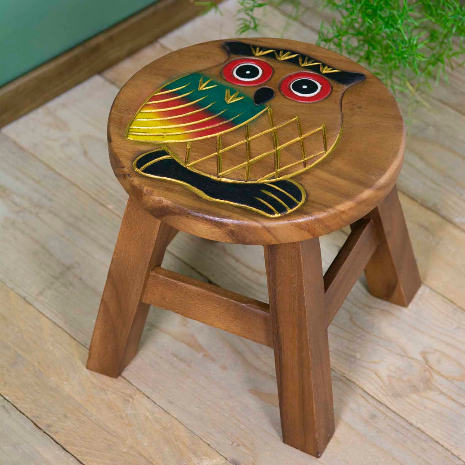 Raintree wood owl stool with hand-carved and painted owl, red-ringed eyes and gold-outlined wings, angled view on wooden floo