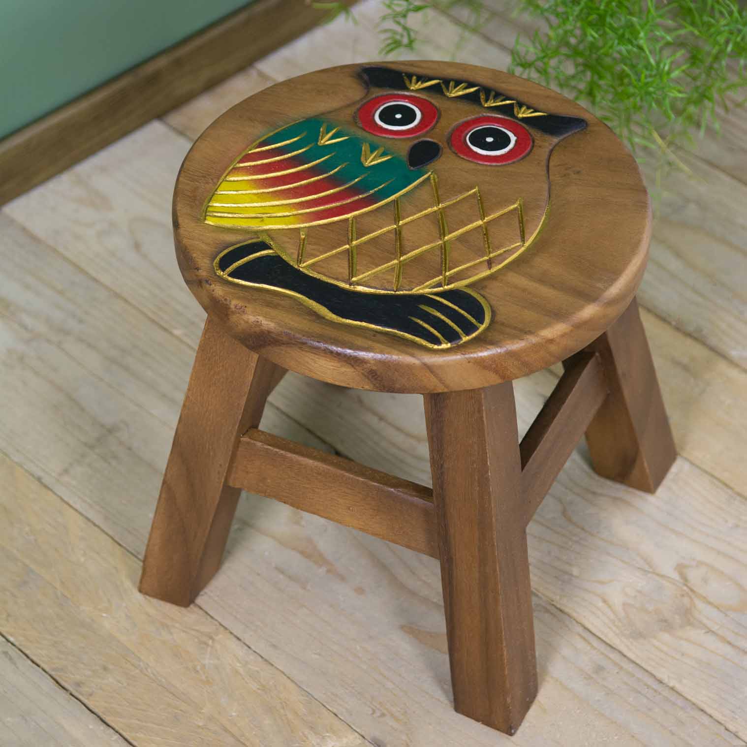 Raintree wood owl stool with hand-carved and painted owl, red-ringed eyes and gold-outlined wings, angled view on wooden floo