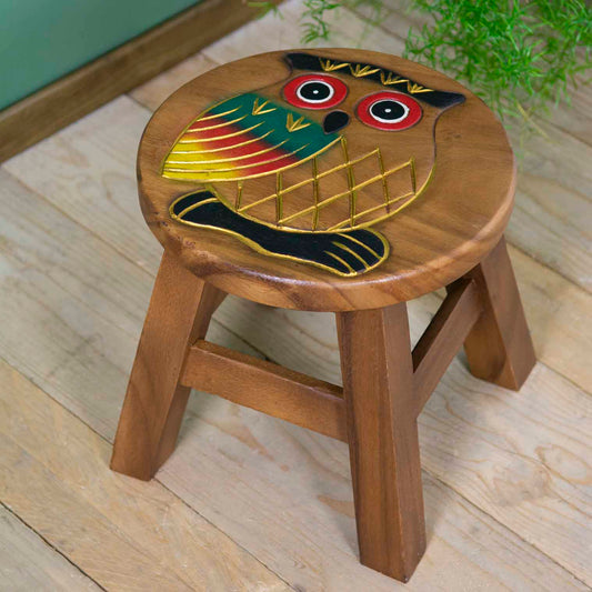 Raintree wood owl stool with hand-carved and painted owl, red-ringed eyes and gold-outlined wings, angled view on wooden floo