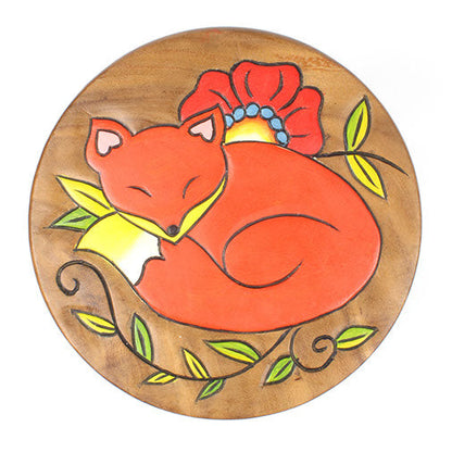Top-down view of Raintree wood stool seat with carved sleeping fox in orange, surrounded by painted green leaves and red popp