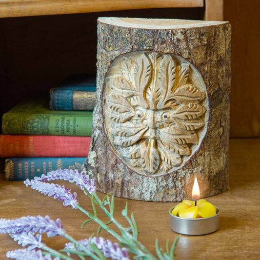 Green Man trunk carving from Indonesia beside a lit candle and lavender sprigs on a wooden shelf