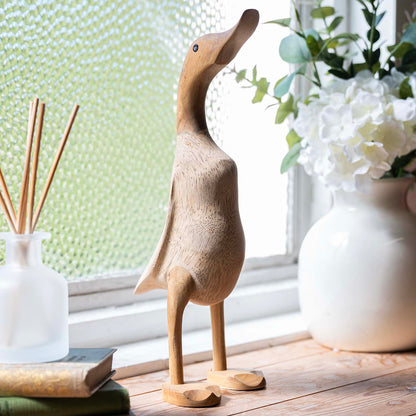 Natural unvarnished bamboo root duck standing on a wooden windowsill beside white flowers, Indonesia