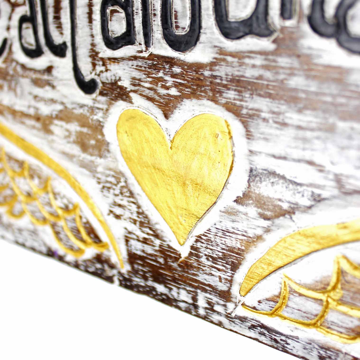 Close-up of carved gold heart at centre of Angel Hugs plaque, with wing detail and whitewashed wood grain visible