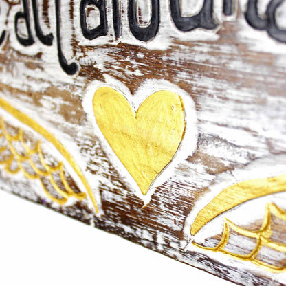 Close-up of carved gold heart at centre of Angel Hugs plaque, with wing detail and whitewashed wood grain visible