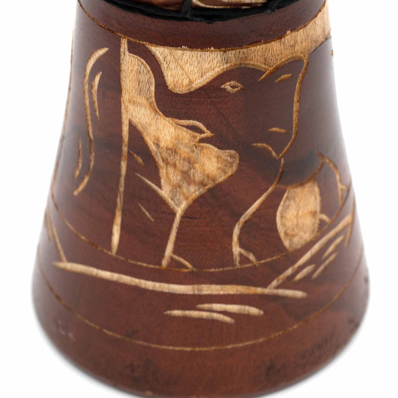 Close-up of carved elephant motif on djembe drum base, pale wood exposed against red-brown stained shell, Indonesia