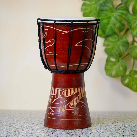 Hand-carved wooden djembe drum with gecko motif carved into reddish-brown base, pale wood details, goatskin head laced with black cord