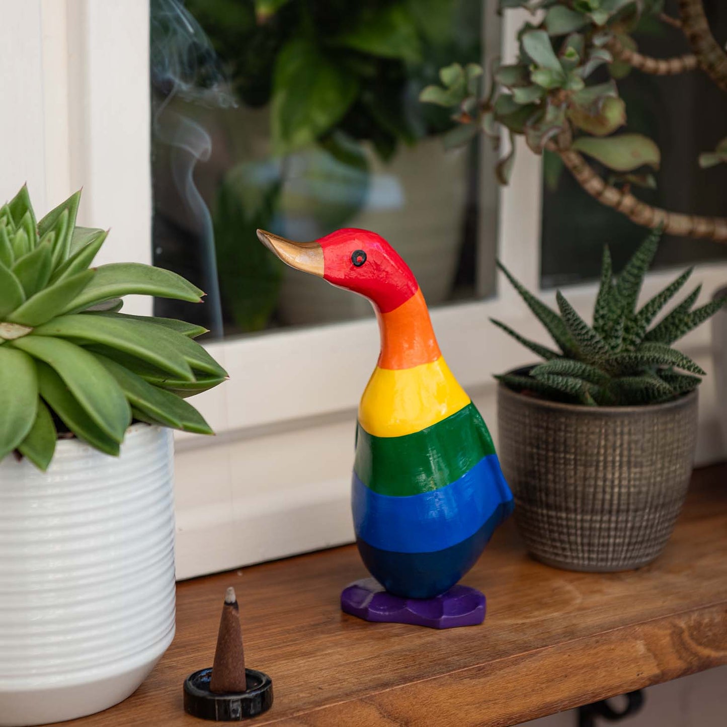 Small rainbow-painted bamboo root duckling on a wooden shelf among succulents, Indonesia