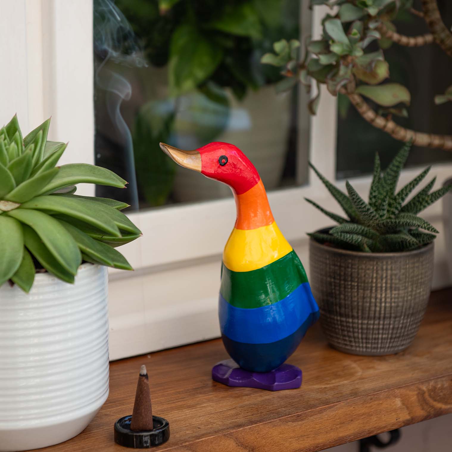 Small rainbow-painted bamboo root duckling on a wooden shelf among succulents, Indonesia