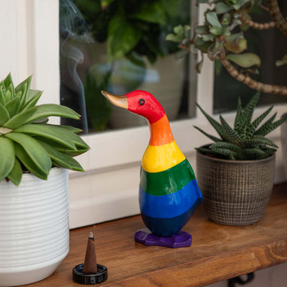 Small rainbow-painted bamboo root duckling on a wooden shelf among succulents, Indonesia