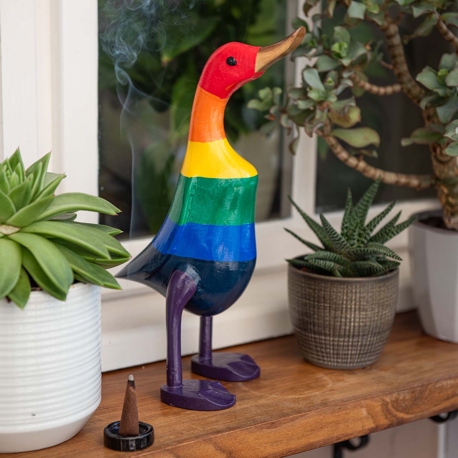 Large rainbow-painted bamboo root duck on a wooden shelf among succulents, Indonesia