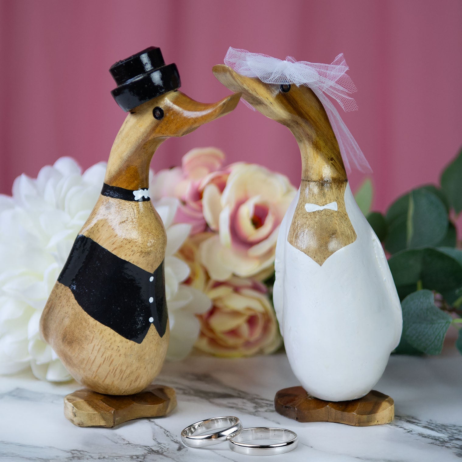 Bamboo root bride duck in white gloss dress with tulle veil beside groom duck, wedding rings in foreground, Bali Indonesia