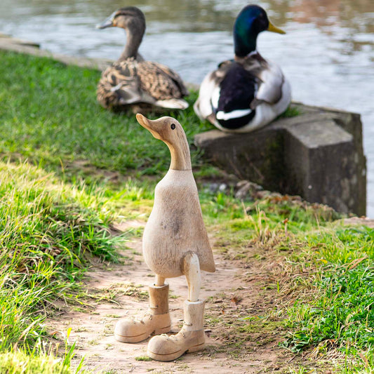 Natural unvarnished bamboo root duck with carved boots, photographed outdoors near a pond with real ducks