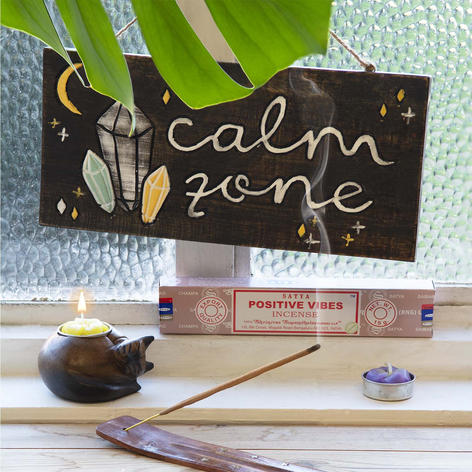 Calm Zone hand-painted wood plaque hanging above incense and candles on a windowsill, showing crystal and star motifs on dark
