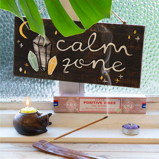 Calm Zone hand-painted wood plaque hanging above incense and candles on a windowsill, showing crystal and star motifs on dark