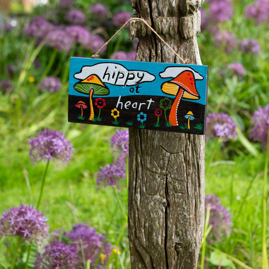 Hippy at Heart hand-painted wood plaque on a wooden post among purple allium flowers, showing toadstool and flower design