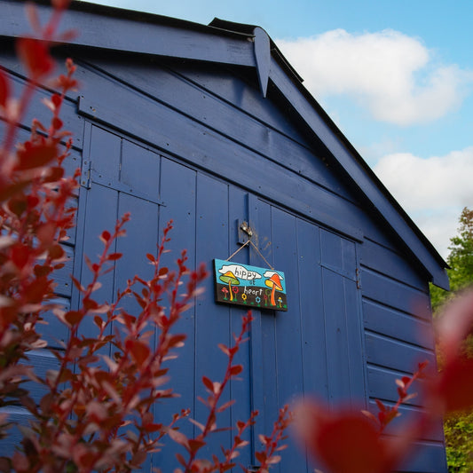 Hippy at Heart plaque hanging on a blue painted shed door, toadstool design visible from a distance