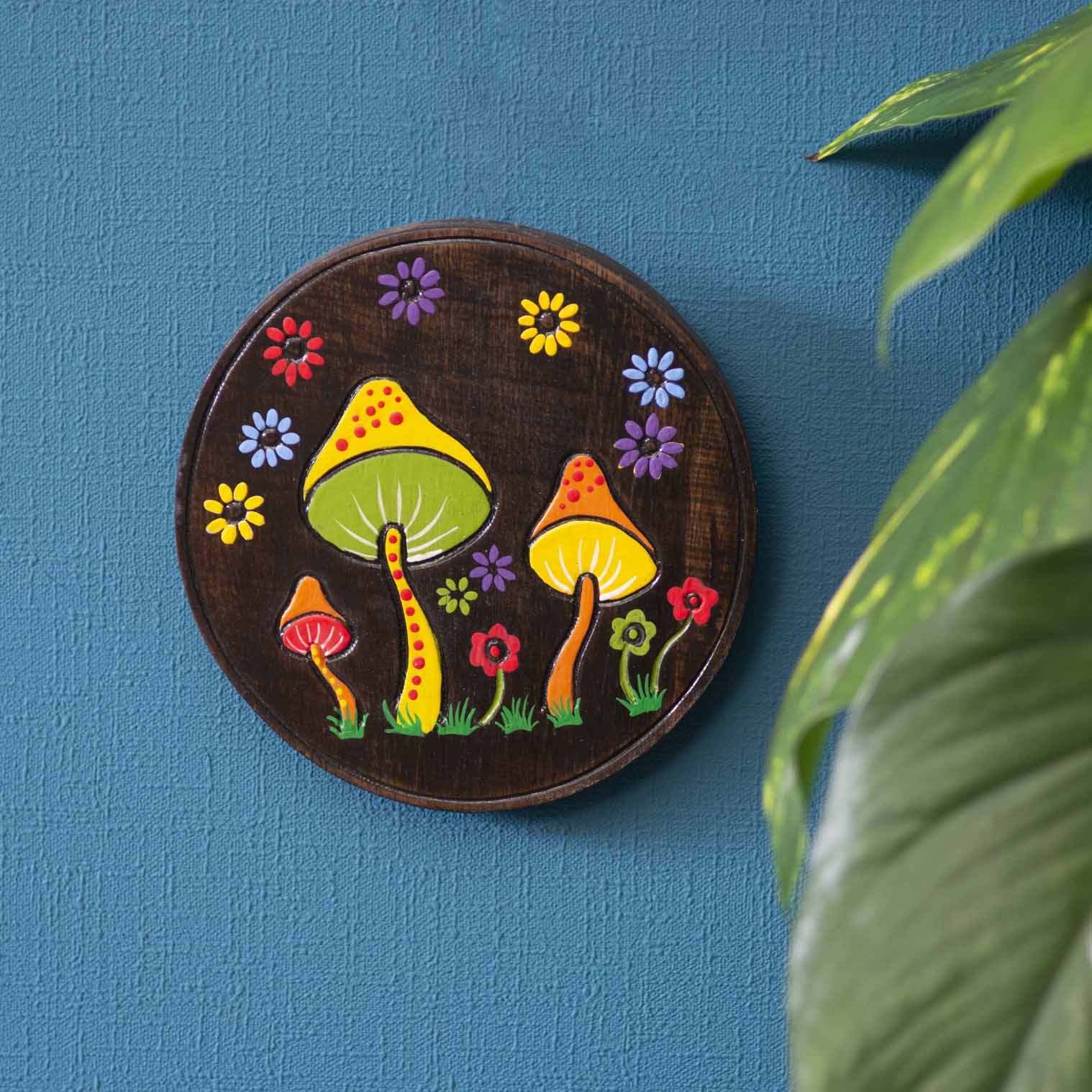 Hand-painted mushroom wood plaque hung on a blue wall, yellow and green toadstool caps on dark stained ground