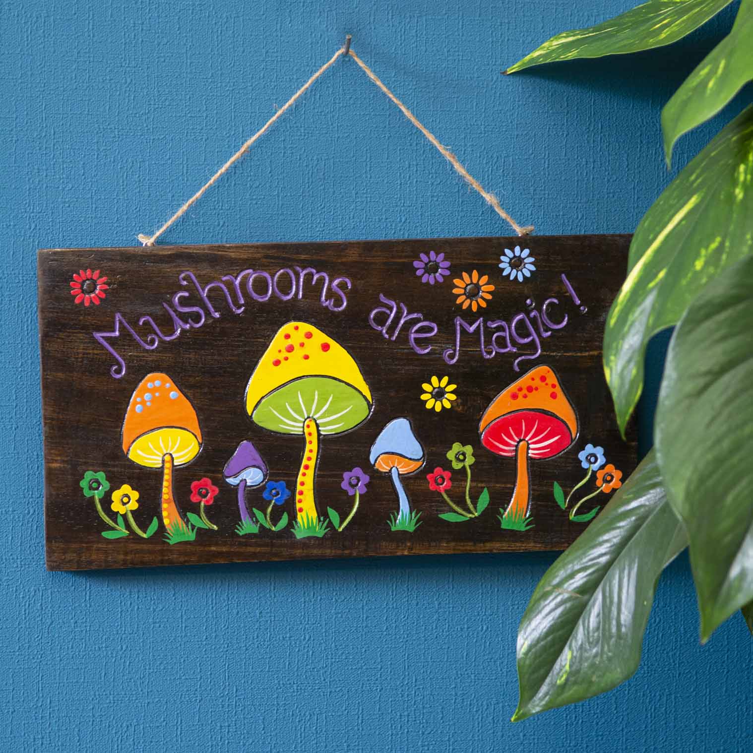 Mushrooms Are Magic wood sign hung on a blue wall, purple lettering and multicolour mushrooms on dark stained plank, Indonesi
