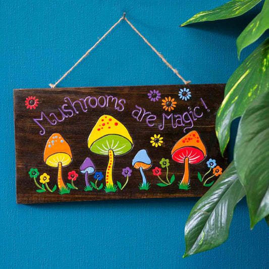Mushrooms Are Magic wood sign hung on a blue wall, purple lettering and multicolour mushrooms on dark stained plank, Indonesi