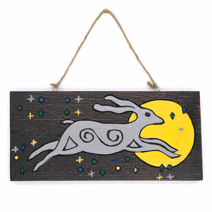 Front view of moon hare wood sign on white background, grey hare with spiral body markings leaping toward a yellow moon, Indo